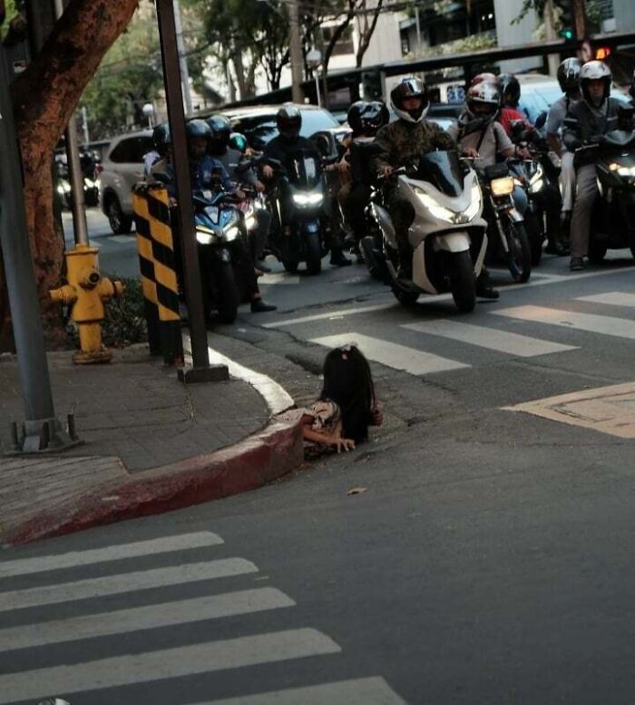 Motorcyclists stopped at a busy urban intersection with a creepy doll stuck in the street gutter highlighting urban hell.