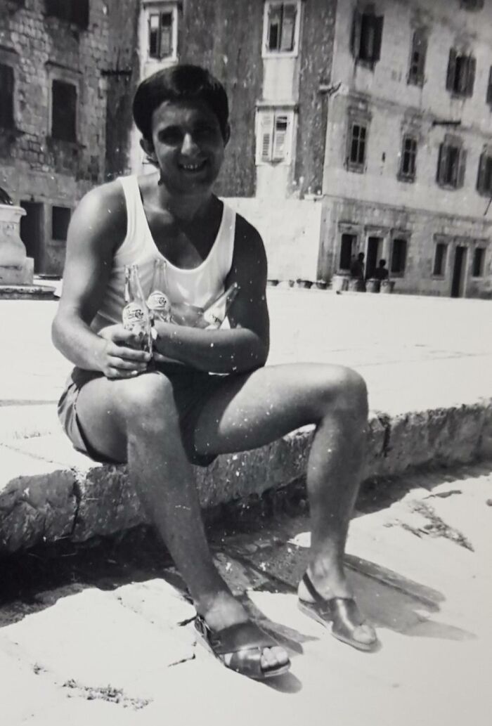 Black and white vintage vacation photo of a man in shorts and sandals sitting outdoors, enjoying drinks before cell phone cameras existed