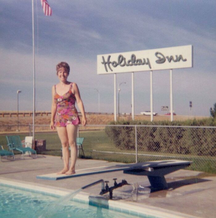 Woman in vintage floral swimsuit standing by motel pool with Holiday Inn sign in background in a classic vacation pic before cell phone cameras.