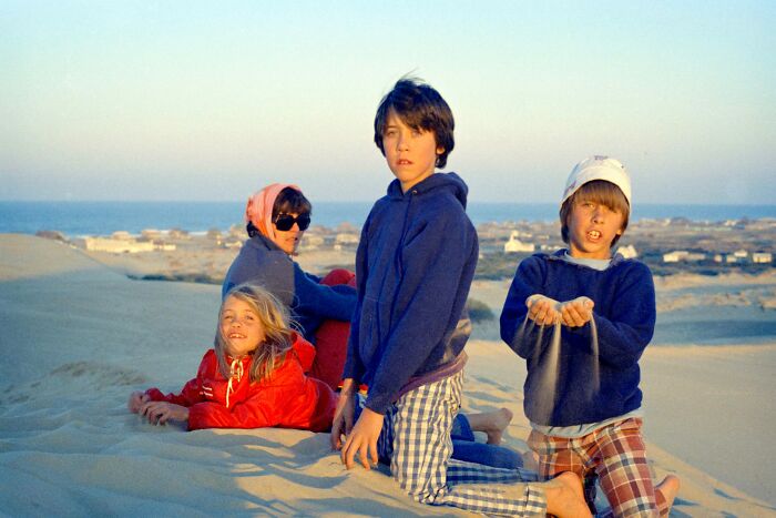 Four kids posing on sandy dunes during a vacation in a time before cell phones had cameras.