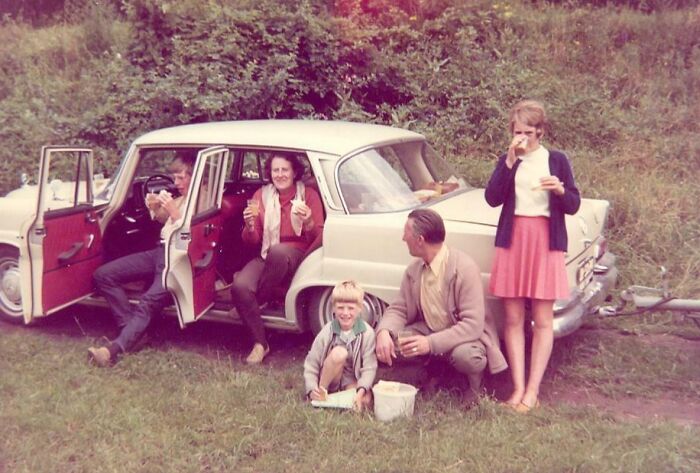Vintage vacation scene with family enjoying snacks near a classic car, capturing vacation pics before cell phones had cameras.