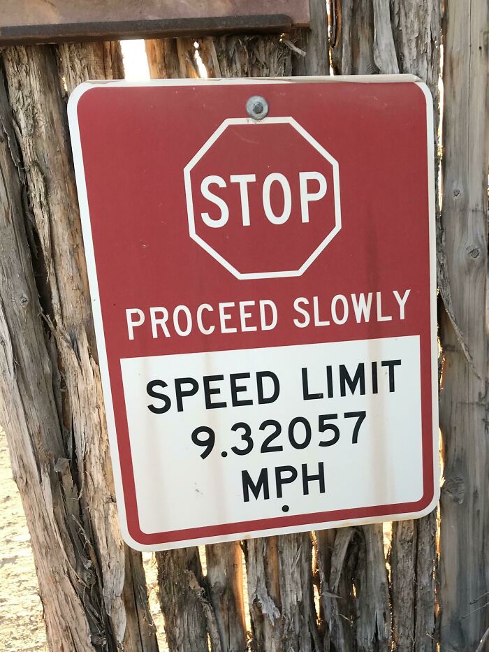 Confusing road sign showing stop and proceed slowly with an unusual speed limit of 9.32057 MPH on wooden post.