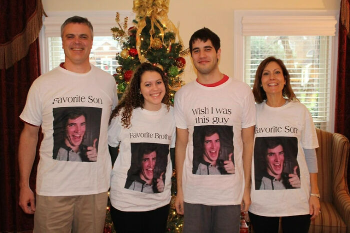 Family wearing matching funny T-shirts posing in front of Christmas tree, capturing cringed family photo moments online.