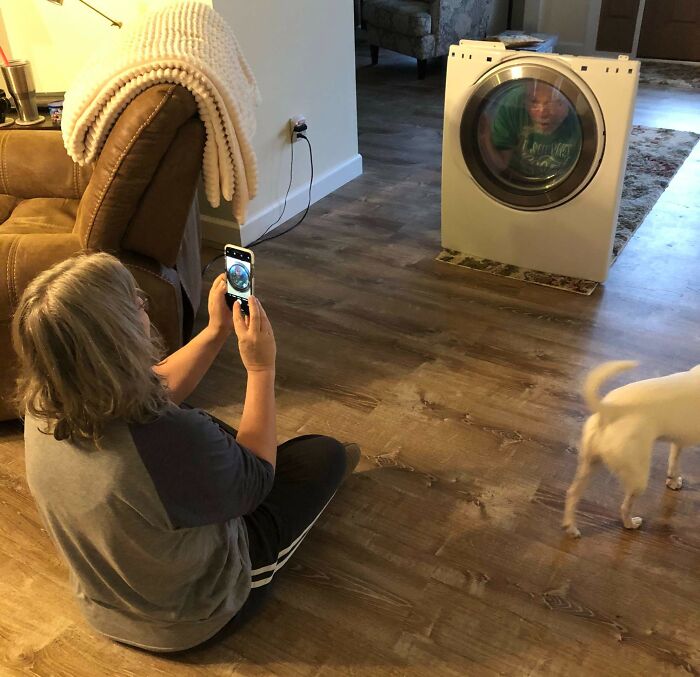 Woman taking a family photo of child inside washing machine drum, a hilarious and cringed family photo moment at home.