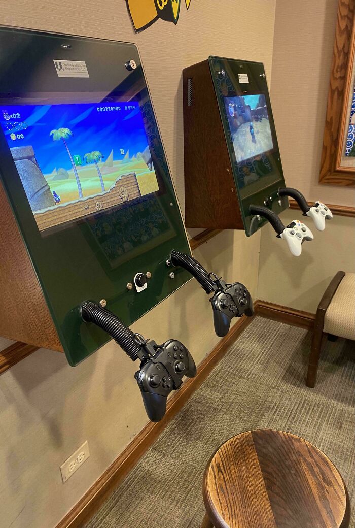 Wall-mounted video game consoles with controllers set up in a waiting room to entertain patients and ease anxiety.
