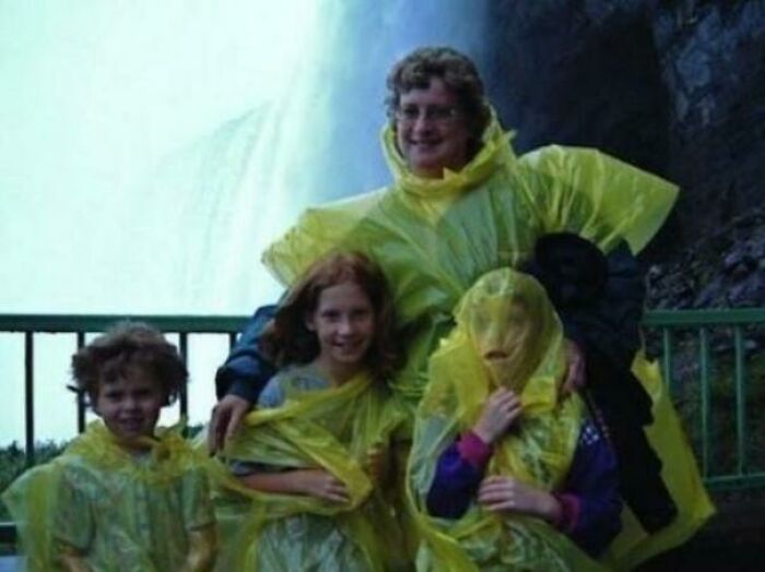 Familia con impermeables amarillos frente a una cascada, en una foto familiar incómoda y memorable.