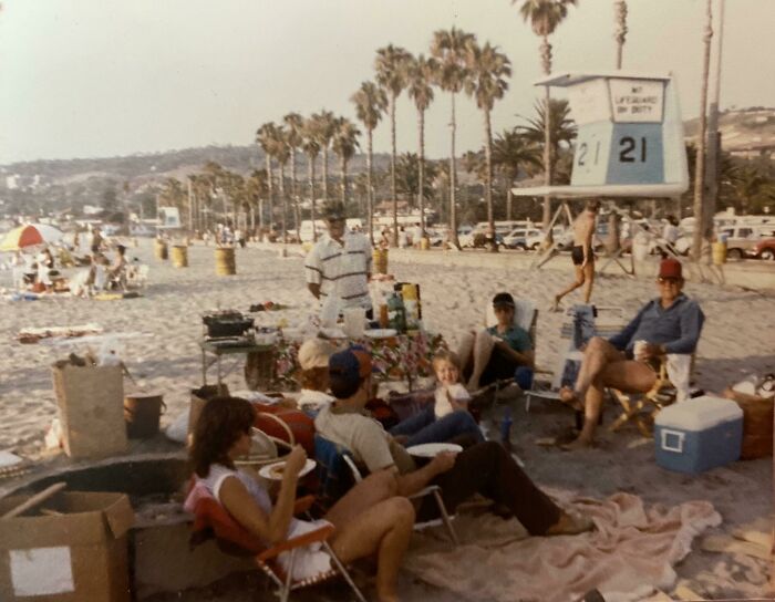 Group of people relaxing on a sunny beach with palm trees and vintage cars, classic vacation pics before cell phone cameras.