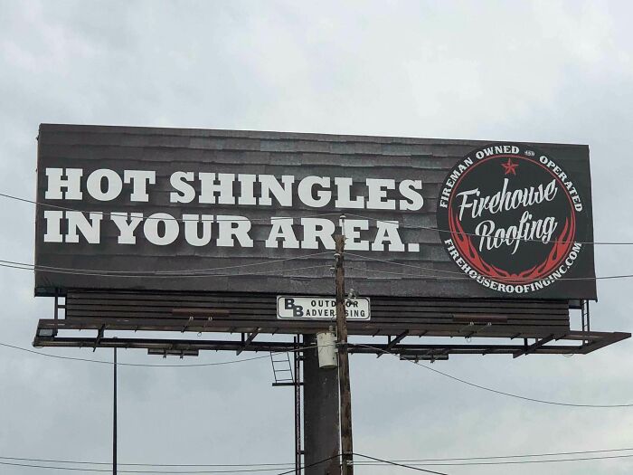Funny and weird billboard advertising roofing with the phrase Hot Shingles in your area on a cloudy day.