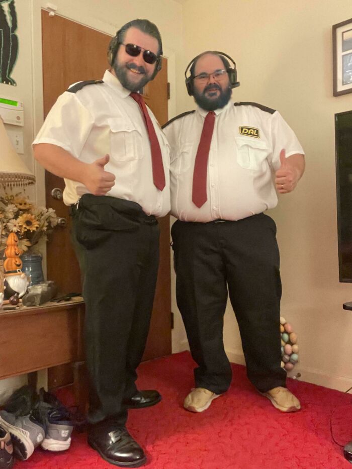 Two men dressed in genius Halloween costumes as pilots giving thumbs up, standing in a living room.