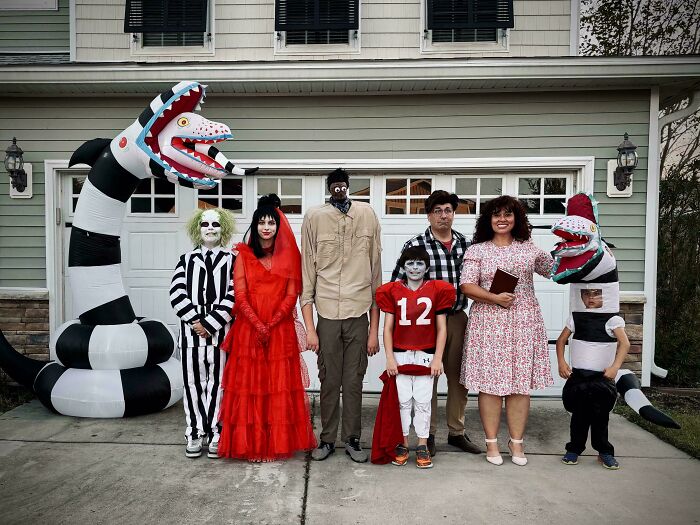 Family dressed in creative Halloween costume ideas posing outside a house with inflatable snake decorations.