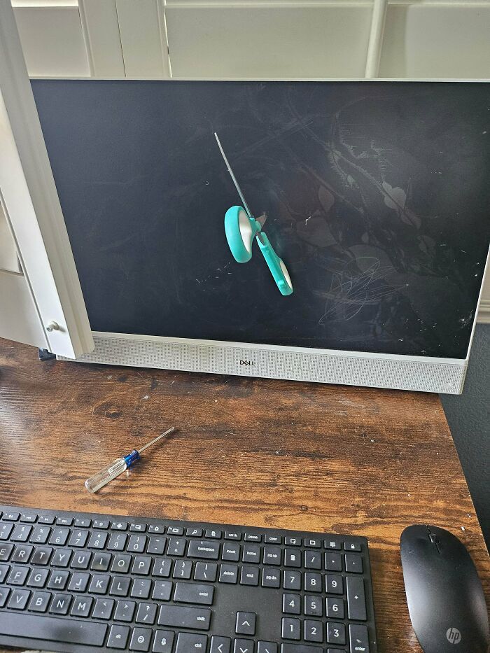 Scissors stuck in a computer monitor screen, showing incorrect handling of electronics and repair tools.