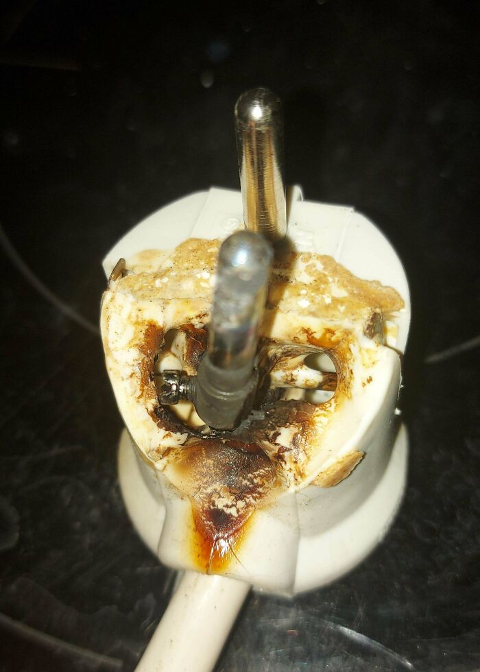 Severely burnt electrical plug with melted plastic and exposed metal, showing dangerous handling of electronics.