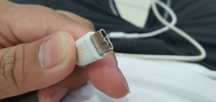 Close-up of a person holding a damaged USB-C cable, illustrating common mistakes in handling electronics and soldering repairs.