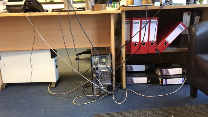 Tangled cables connected to a desktop computer under a desk, showing poor handling of electronics and wiring.
