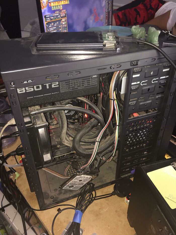 Open computer case with tangled cables and hard drive resting loosely, showing improper handling of electronics and soldering risks.