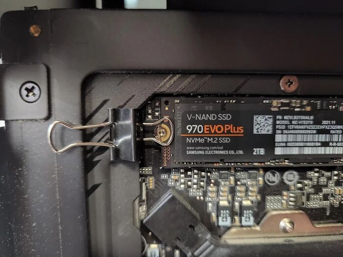 Close-up of electronics inside a device with a binder clip used to hold an M.2 NVMe SSD in place, illustrating wrong soldering.