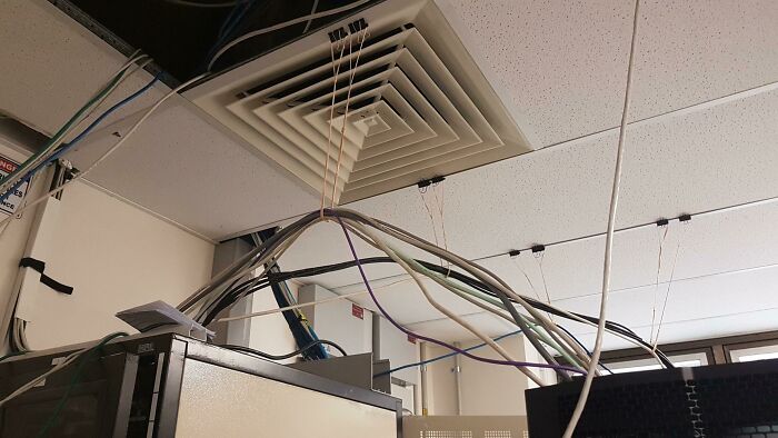 Tangled and unsupported cables hanging from ceiling in an office server room, showing poor handling of electronics.