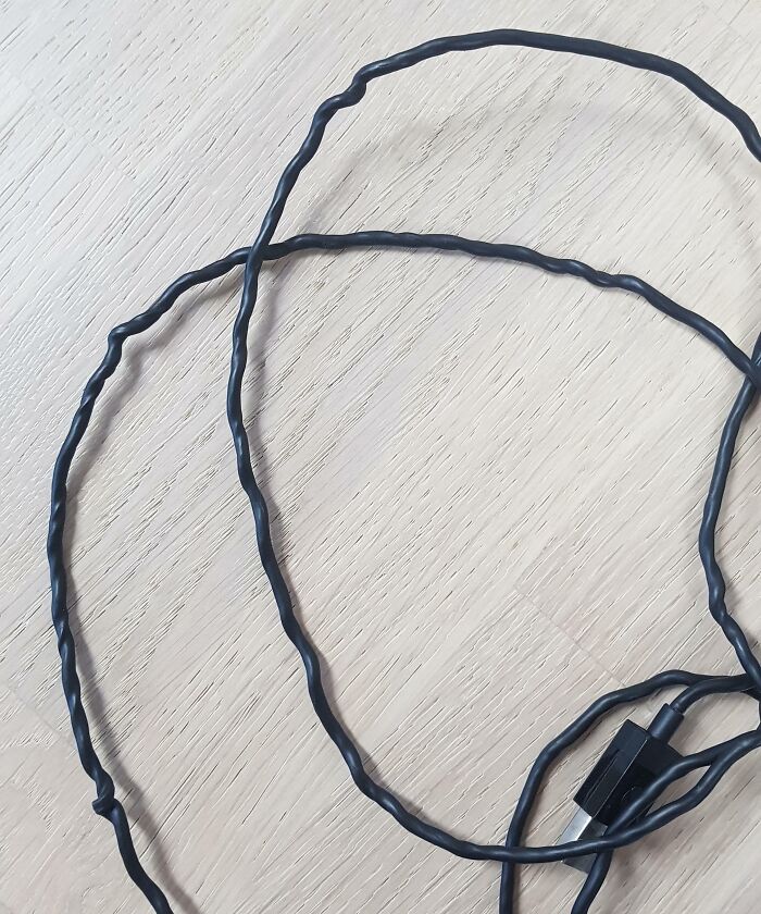 Twisted and damaged black electronic cable lying on a wooden surface, illustrating improper handling of electronics.