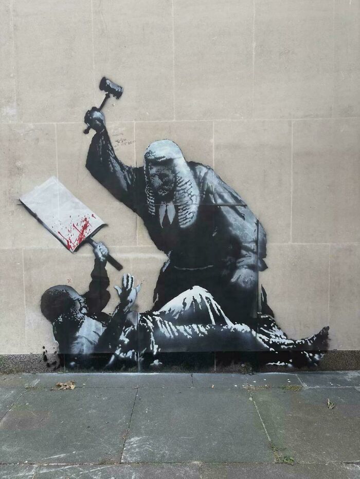 Street art depicting a judge raising a gavel over a person holding a bloody cleaver on a city wall.