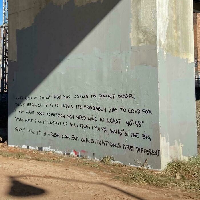 Street art graffiti with a handwritten message about paint and adhesion on a weathered concrete wall outdoors.