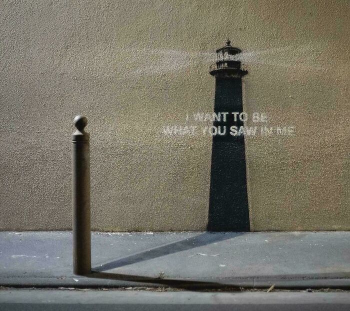 Shadow art of a bollard transformed into a lighthouse with the message I want to be what you saw in me street art.
