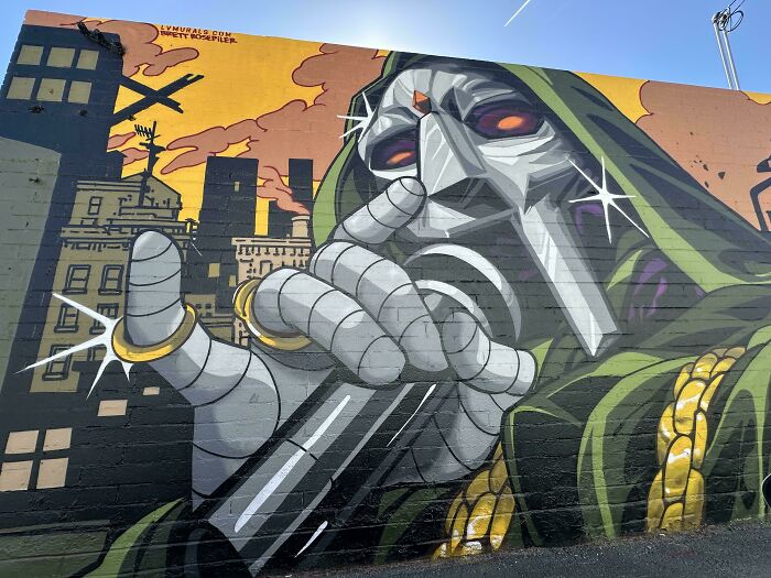 Powerful street art depicting a robotic figure with glowing eyes and metallic hand against an urban sunset background.
