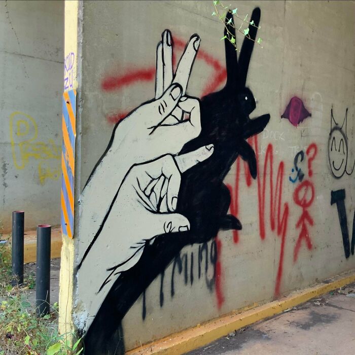 Street art mural of hands creating a rabbit shadow on a wall with vibrant graffiti background.