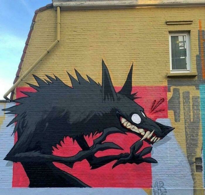 Street art mural of a fierce black wolf with sharp teeth on a colorful brick wall in an urban setting.