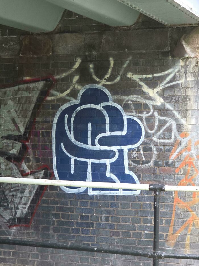 Abstract blue and white street art of two figures embracing on a brick wall with colorful graffiti around it.