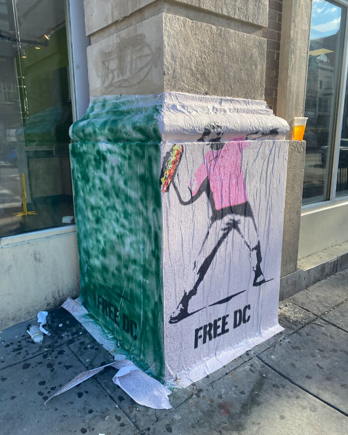 Street art on a city corner showing a figure in a pink shirt with the text Free DC in an urban setting.
