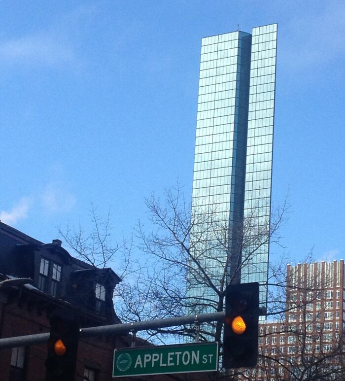 Tall glass building with a reflective surface appearing to bend, seen behind traffic lights and an Appleton Street sign.
