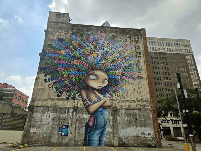 Large colorful street art of a girl with words as hair on an urban building wall, showcasing powerful street art style.