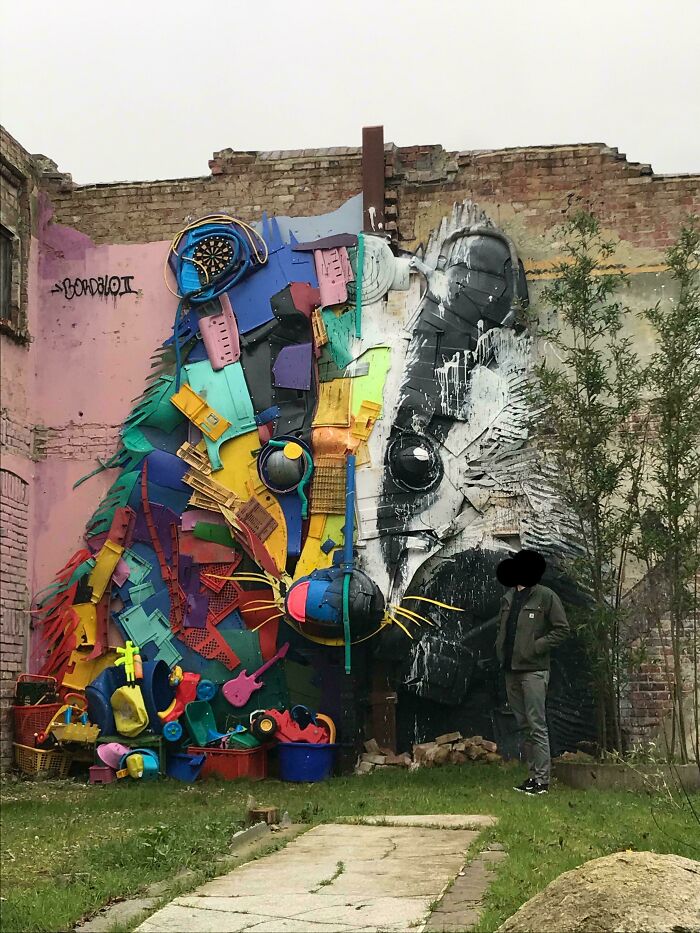 Large colorful and black-and-white street art of a rodent on a brick wall with a person standing nearby in an outdoor setting.