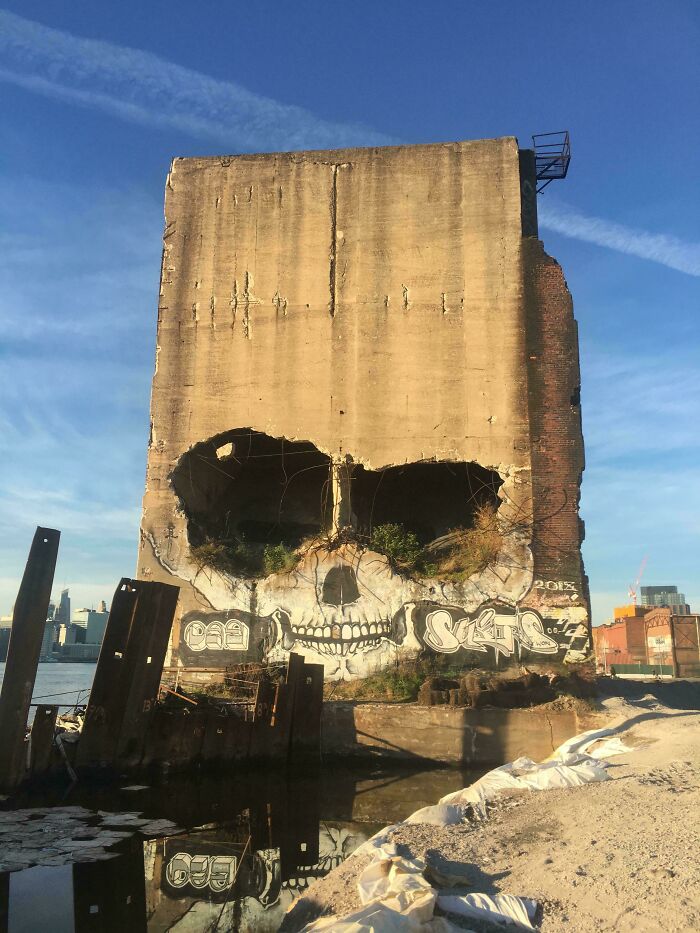 Street art skull mural painted on a large concrete building near an urban waterfront.