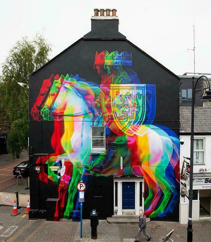 Colorful and powerful street art of a knight on horseback painted on a black building wall in an urban setting.