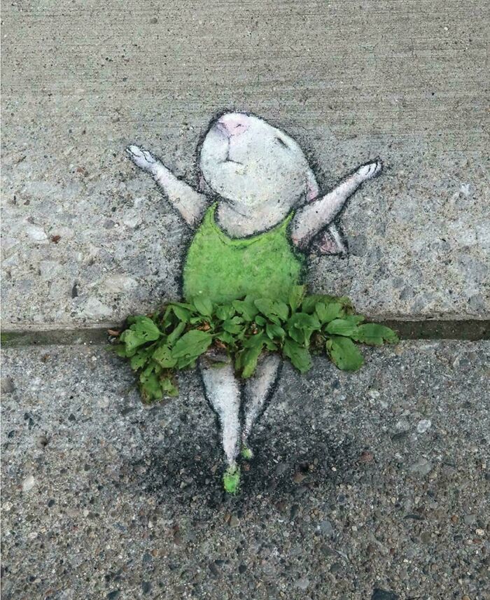 Street art of a white rabbit with a green dress and leaves as a tutu, painted on concrete pavement with a joyful pose.