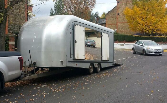 Trailer attached to a pickup truck with an open side door, blending unusually with the street and surroundings in a real scene.