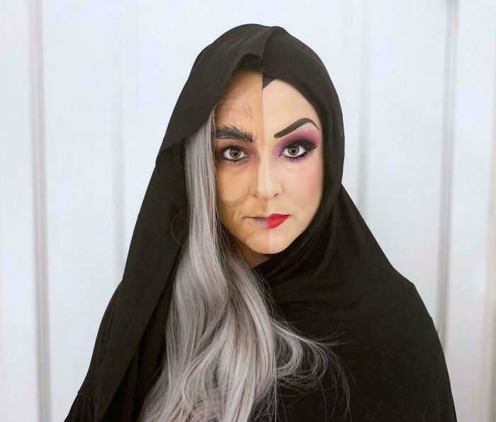 Person in creative Halloween costume with half face old woman makeup and half with colorful makeup wearing black hooded cloak