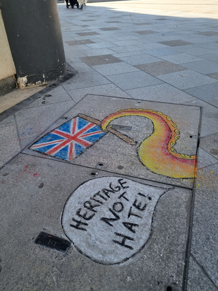Street art on pavement showing a Union Jack flag and an octopus arm with a message Heritage Not Hate near a street corner.