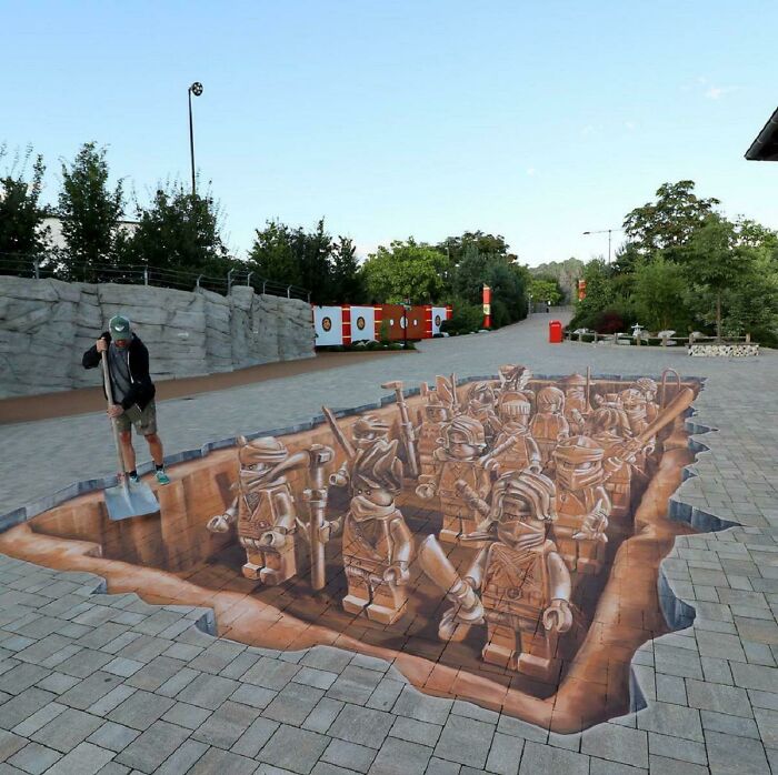 3D street art showing a group of warriors in a deep trench on a paved pathway with a person standing nearby.