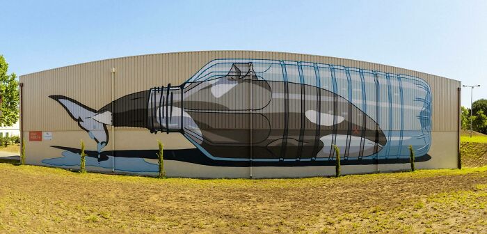 Large street art mural of an orca whale trapped inside a plastic bottle on an outdoor wall, showcasing powerful street art.