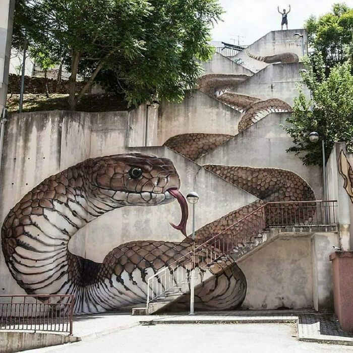 Large street art mural of a realistic snake winding around outdoor staircases in an urban setting.