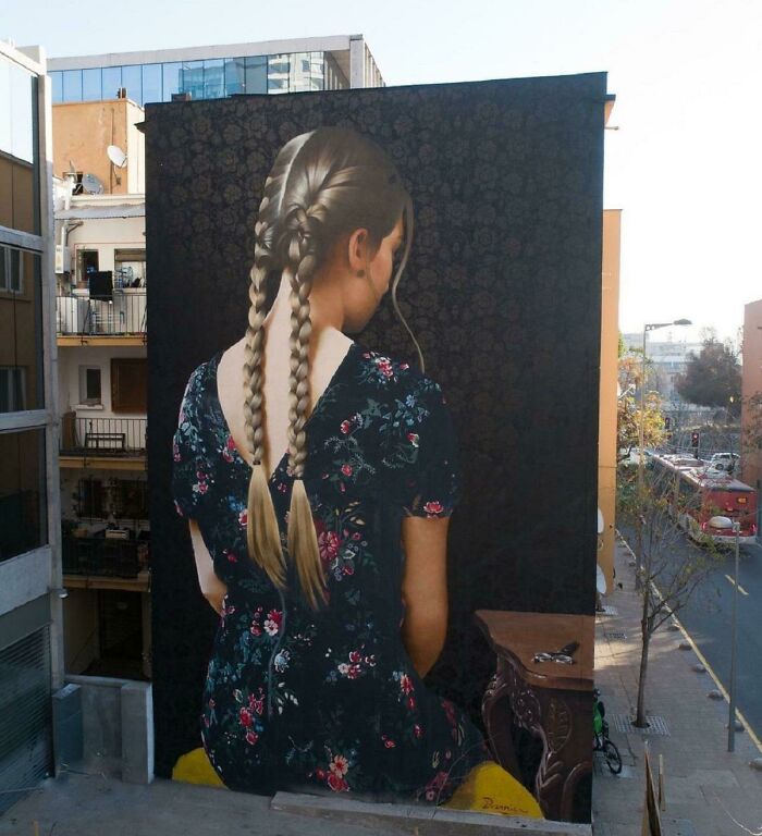 Large street art mural of a girl with braided hair in a floral dress, showcasing beautiful and powerful street art worldwide.