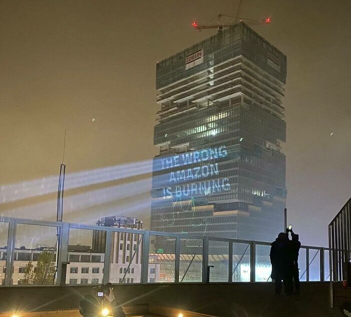 Powerful street art projection on a skyscraper at night highlighting an environmental message about the Amazon burning.