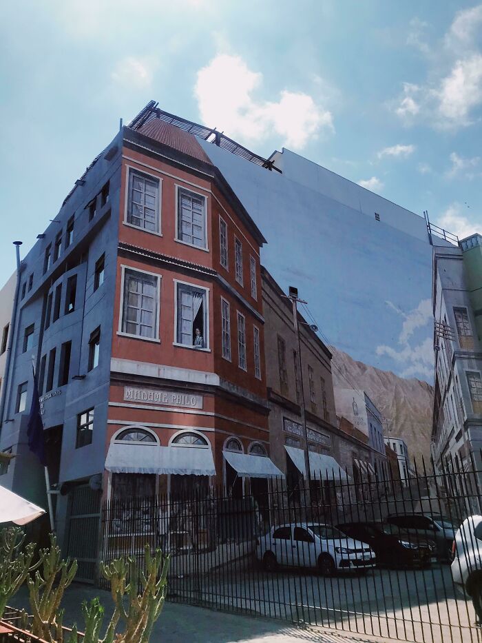 Street art mural on building facade creating an optical illusion of extended buildings with detailed windows and awnings.