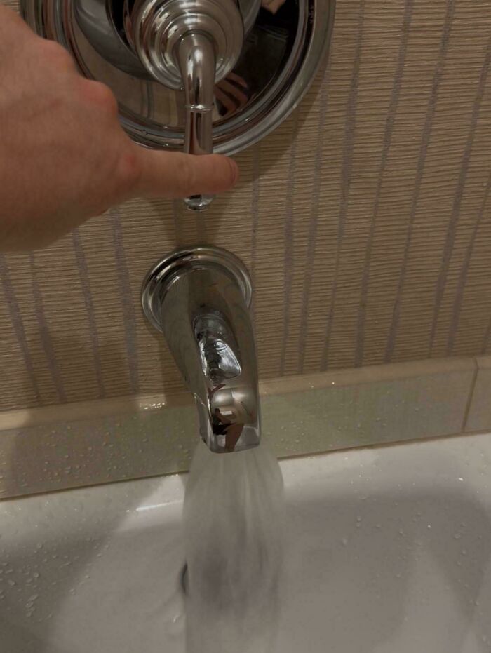 Hand turning shower handle while water flows from bathtub faucet, showing a mildly infuriating plumbing setup.