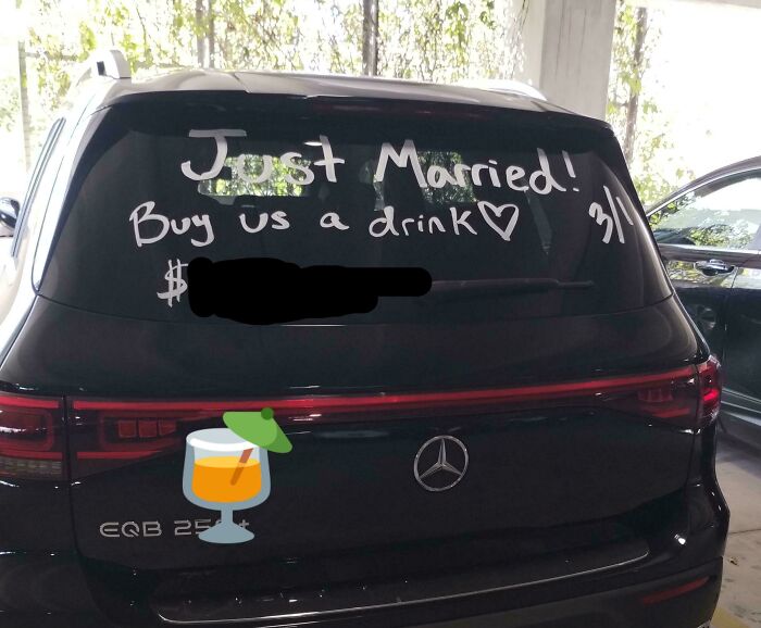 Black Mercedes SUV with "Just Married! Buy us a drink" written on the rear window, a mildly infuriating photo testing patience.