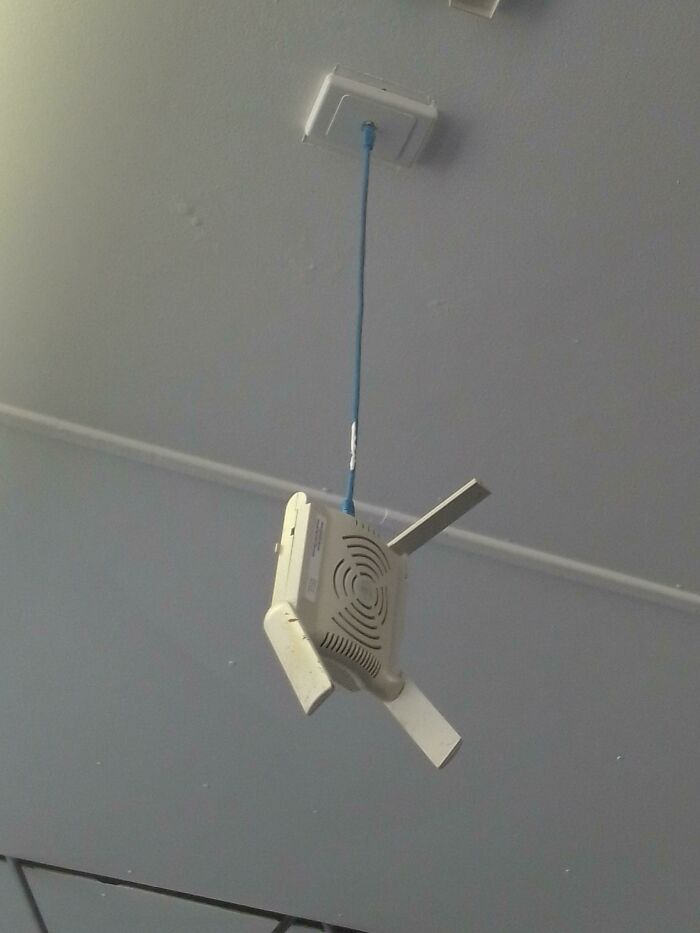Poorly handled electronics with a wireless router hanging from the ceiling by a twisted cable in an unsafe DIY setup.