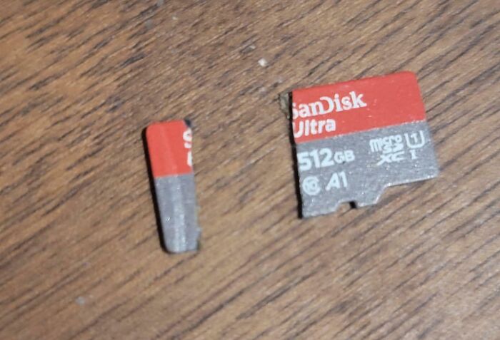 Broken SanDisk Ultra 512GB microSD card split into two pieces on a wooden surface, mishandled electronics example.