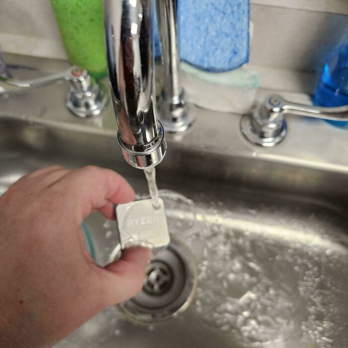 Hand holding a Ryzen CPU under running faucet, a painful example of handling electronics the wrong way.